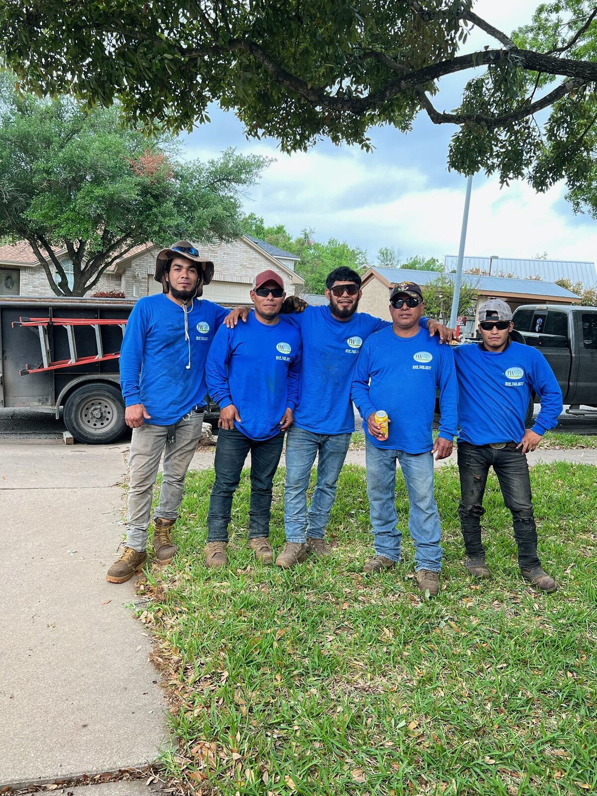JW Tree and Land Service crew in matching blue company shirts standing on a lawn in front of their truck and trailer